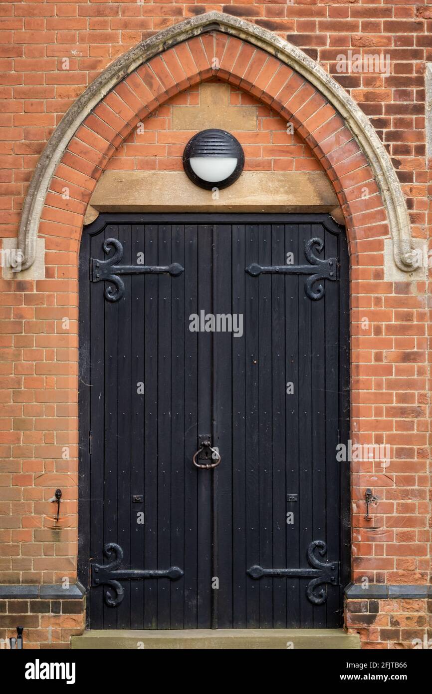 Pesante porta chiesa nera in legno con bande di ferro sotto a. arco in mattoni Foto Stock