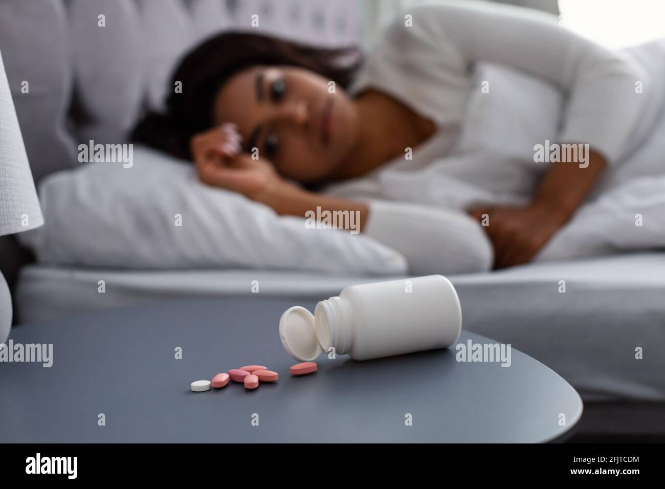 Donna nera che soffre di insonnia, pillole sul tavolo Foto Stock