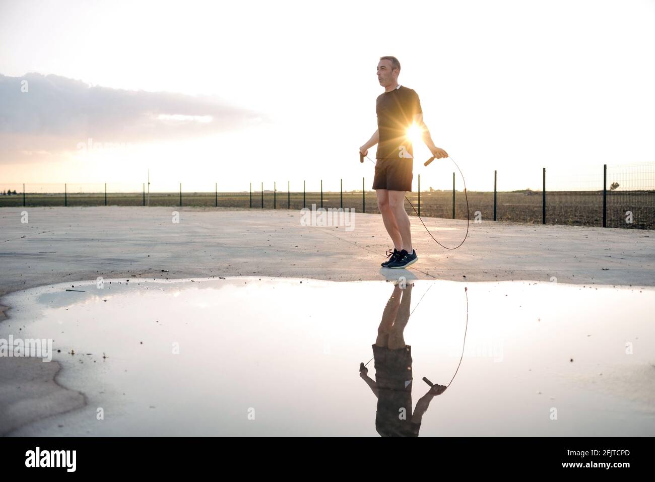 Concetto: sport. Atleta uomo all'aperto. Corda che salta. Retroilluminazione al tramonto. Riflesso nell'acqua di un puddle. Stella solare, sunstar Foto Stock