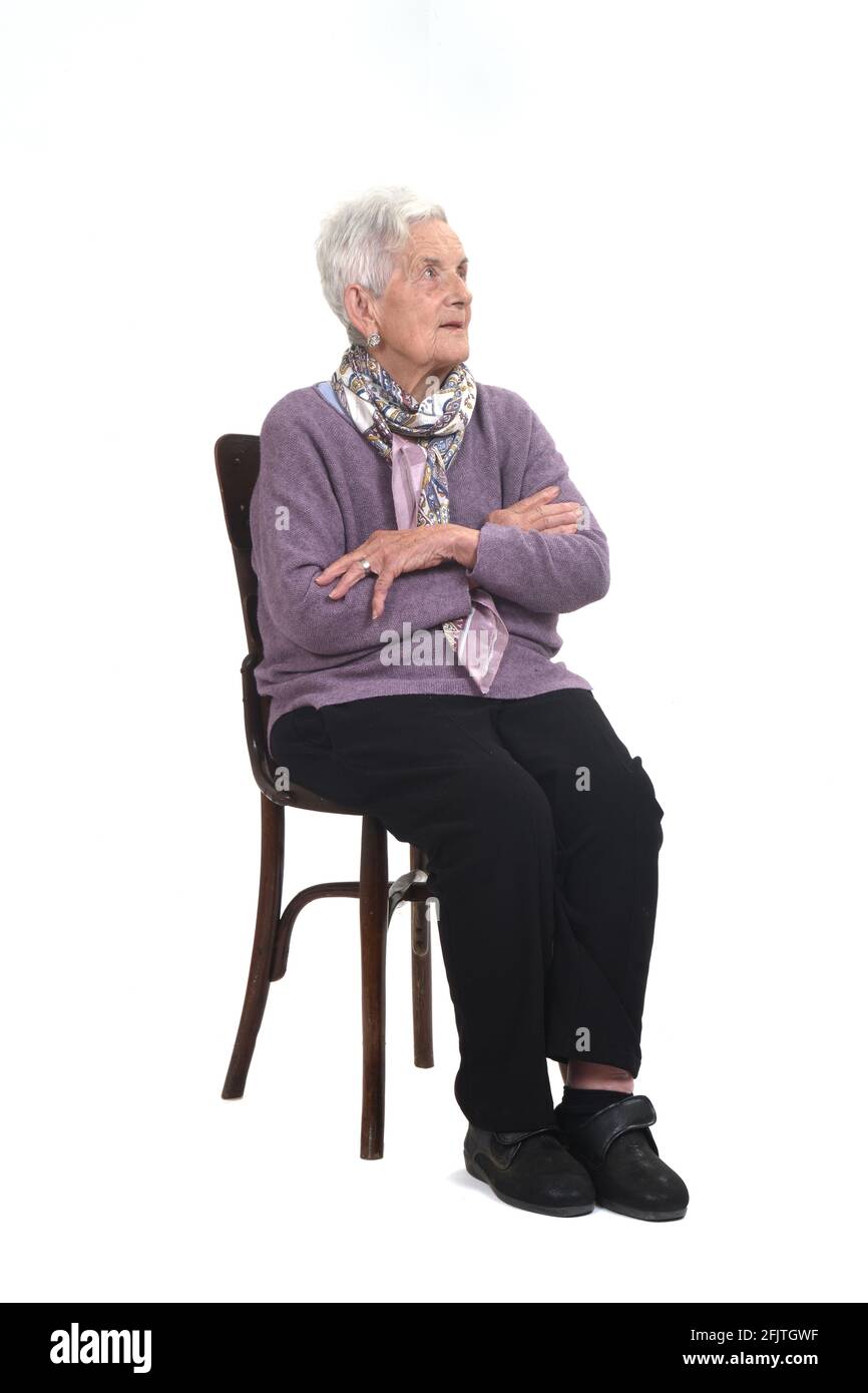 vista di una donna senir seduta sulla sedia che guarda in alto e le braccia incrociate su sfondo bianco Foto Stock