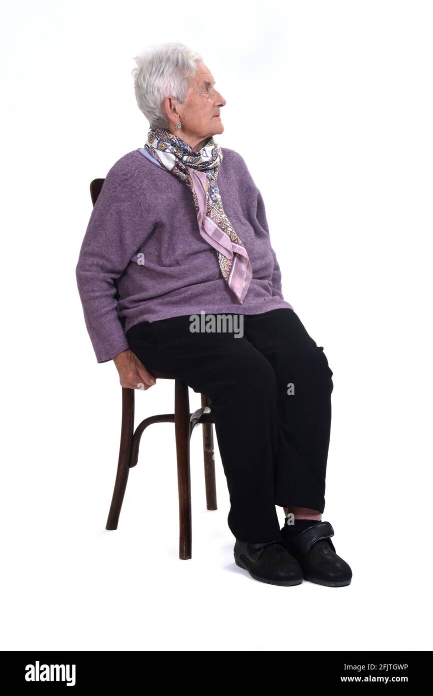 vista di una donna senir seduta su sedia che guarda in su, seria su sfondo bianco Foto Stock