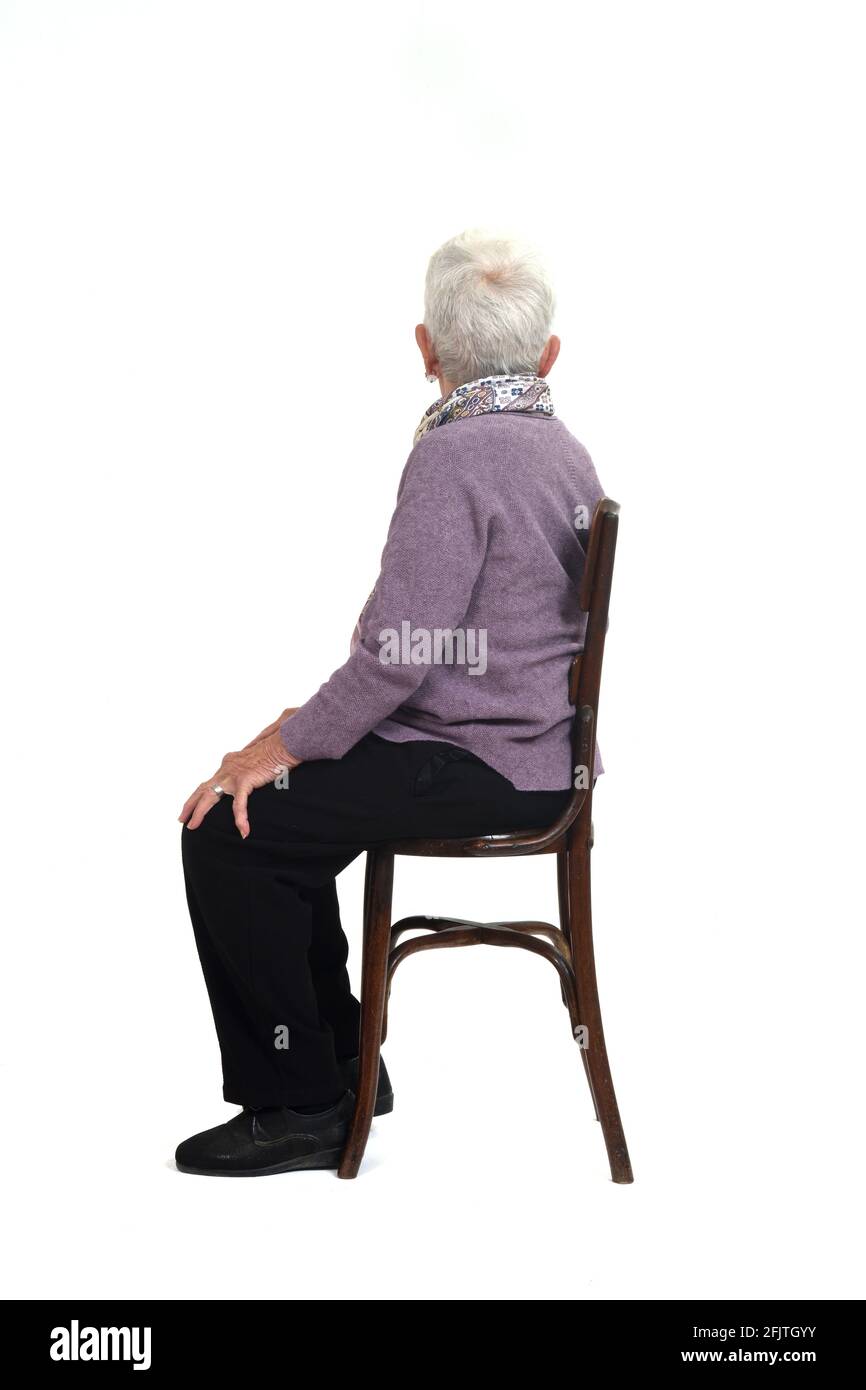 vista laterale di una donna senir seduta su una sedia che guarda via su sfondo bianco Foto Stock