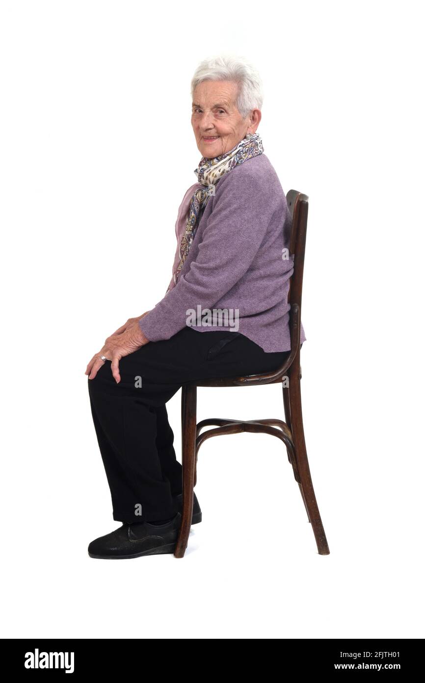 vista laterale di una donna senir seduta su una sedia sorridente e guardando la fotocamera su sfondo bianco Foto Stock