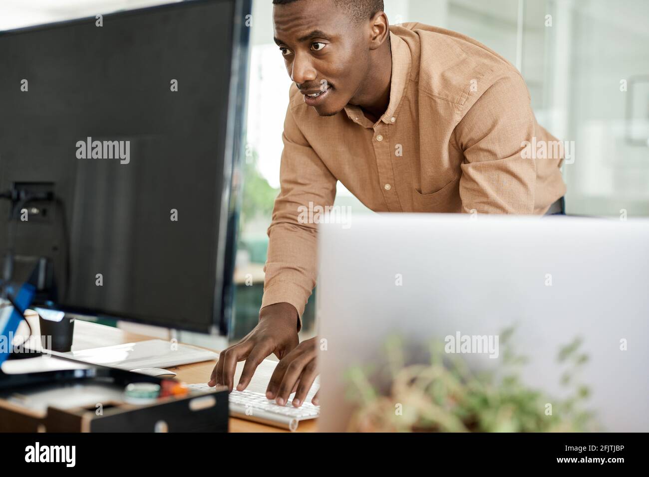 Uomo d'affari africano che lavora su una tastiera per computer alla sua scrivania Foto Stock