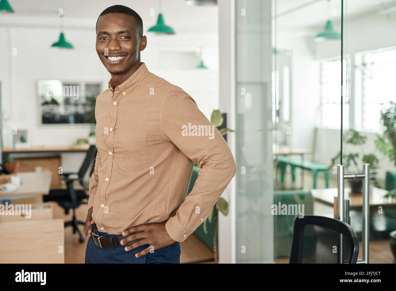 Sorridente giovane uomo d'affari africano in piedi da solo in un ufficio Foto Stock