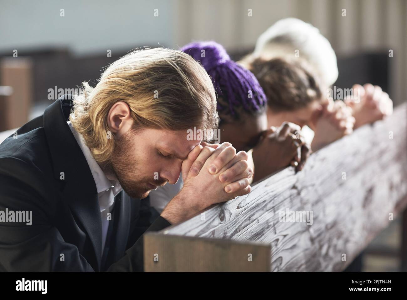 Gruppo di persone che si siedono in fila con gli occhi chiusi e pregare insieme nella chiesa Foto Stock