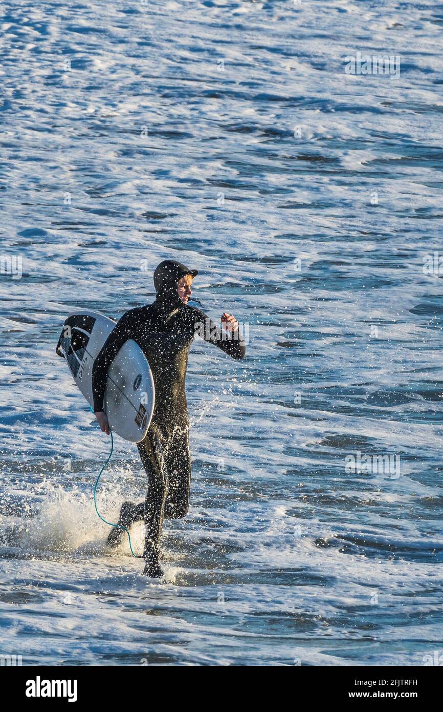 Un appassionato di surf che porta la sua tavola da surf e corre in mare a Fistral a Newquay in Cornovaglia. Foto Stock