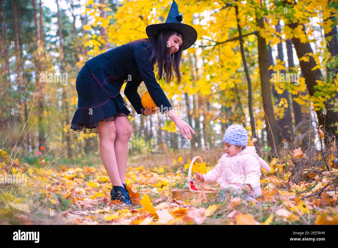 donna strega gioca con un bambino piccolo nella foresta d'autunno. halloween concetto costumi. strega e coniglietto. concetto di amici madre e figlia Foto Stock
