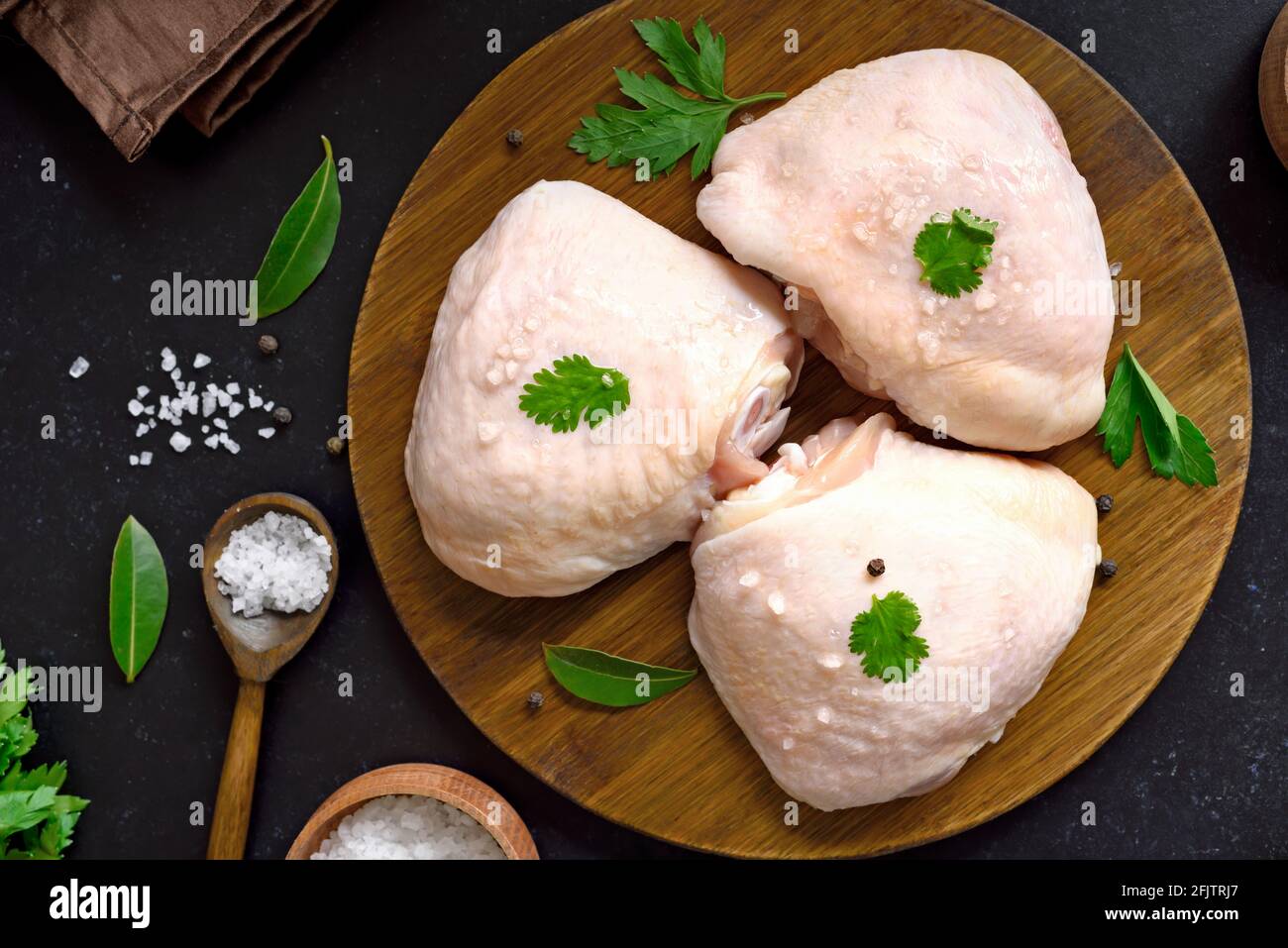 Coscia di pollo cruda su tagliere di legno su sfondo scuro. Vista dall'alto, disposizione piatta Foto Stock