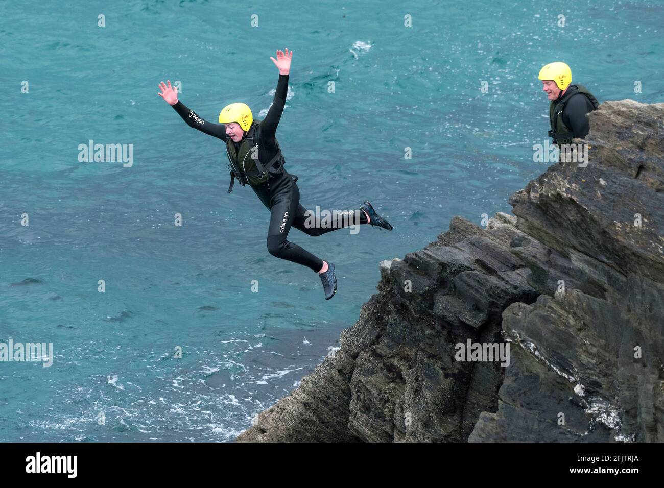 Un giovane turista che salta in mare dalle rocce in un viaggio di coastering intorno a Towan Head a Newquay in Cornovaglia. Foto Stock