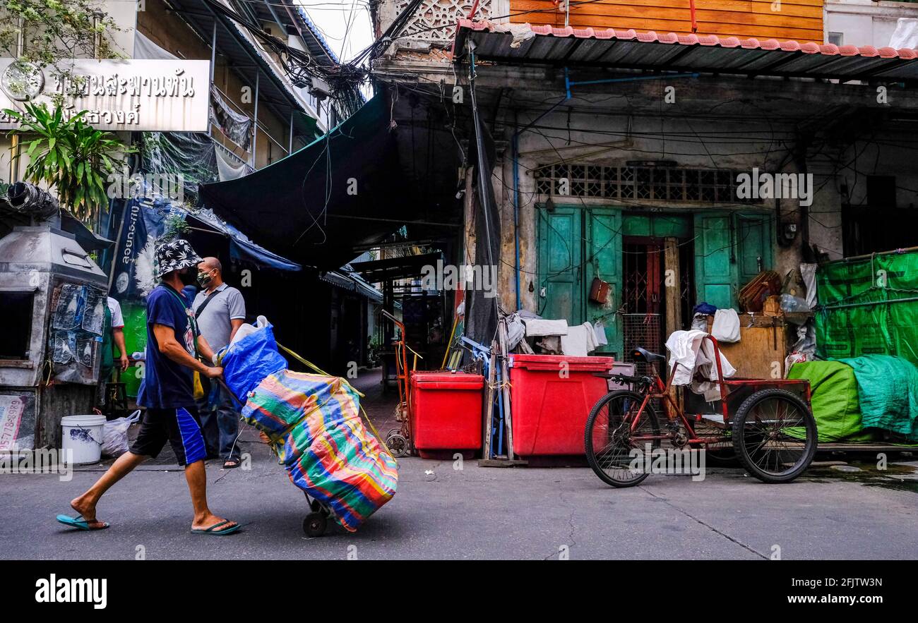 Un portiere maschile spinge un piccolo trolley lungo un vicolo nella zona di Chinatown a Bangkok, Thailandia Foto Stock