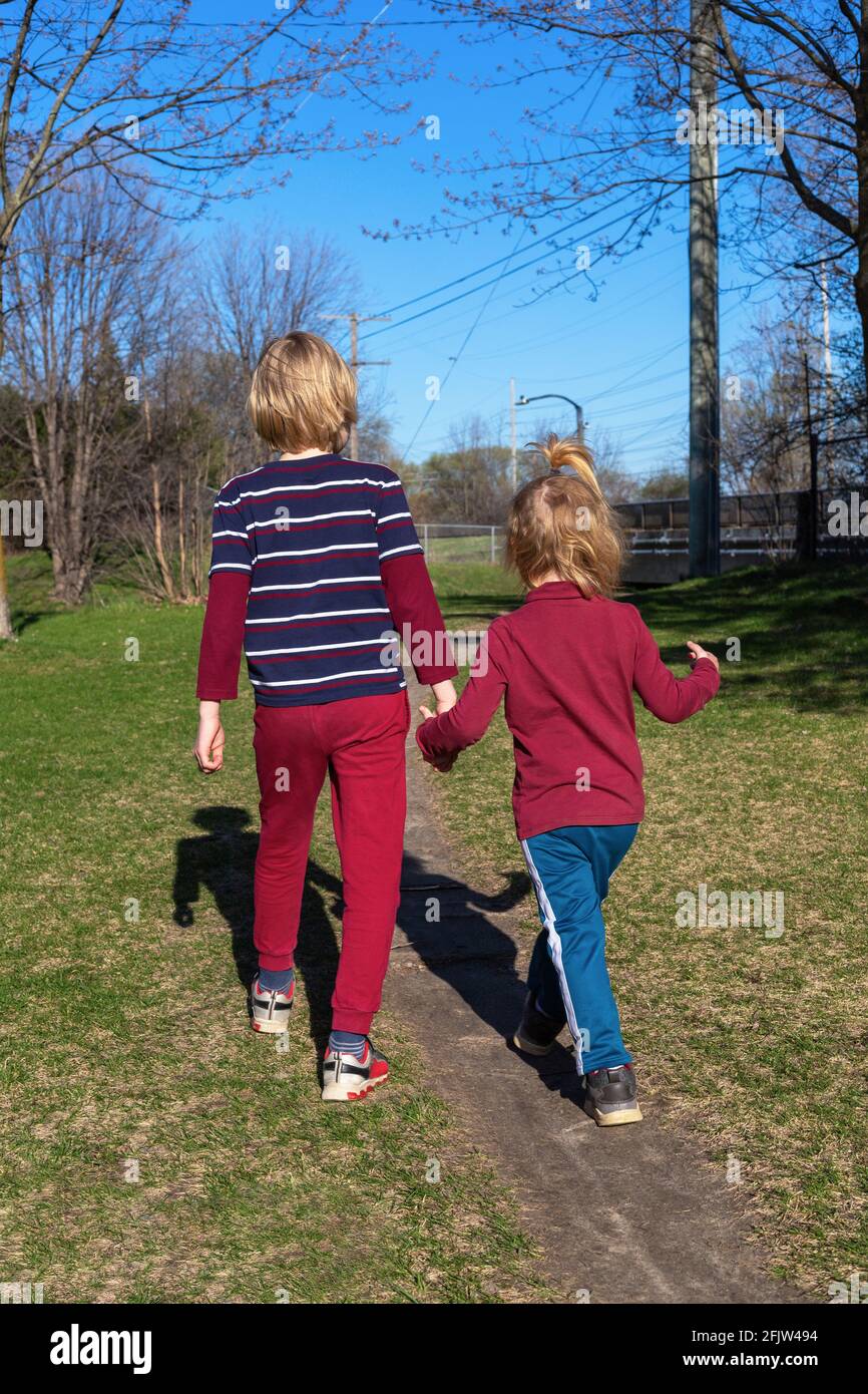 Bambini che camminano nel parco in primavera. Fratelli che tengono le mani. Concetto di famiglia e amicizia. Fratello e sorella insieme da dietro. Foto Stock