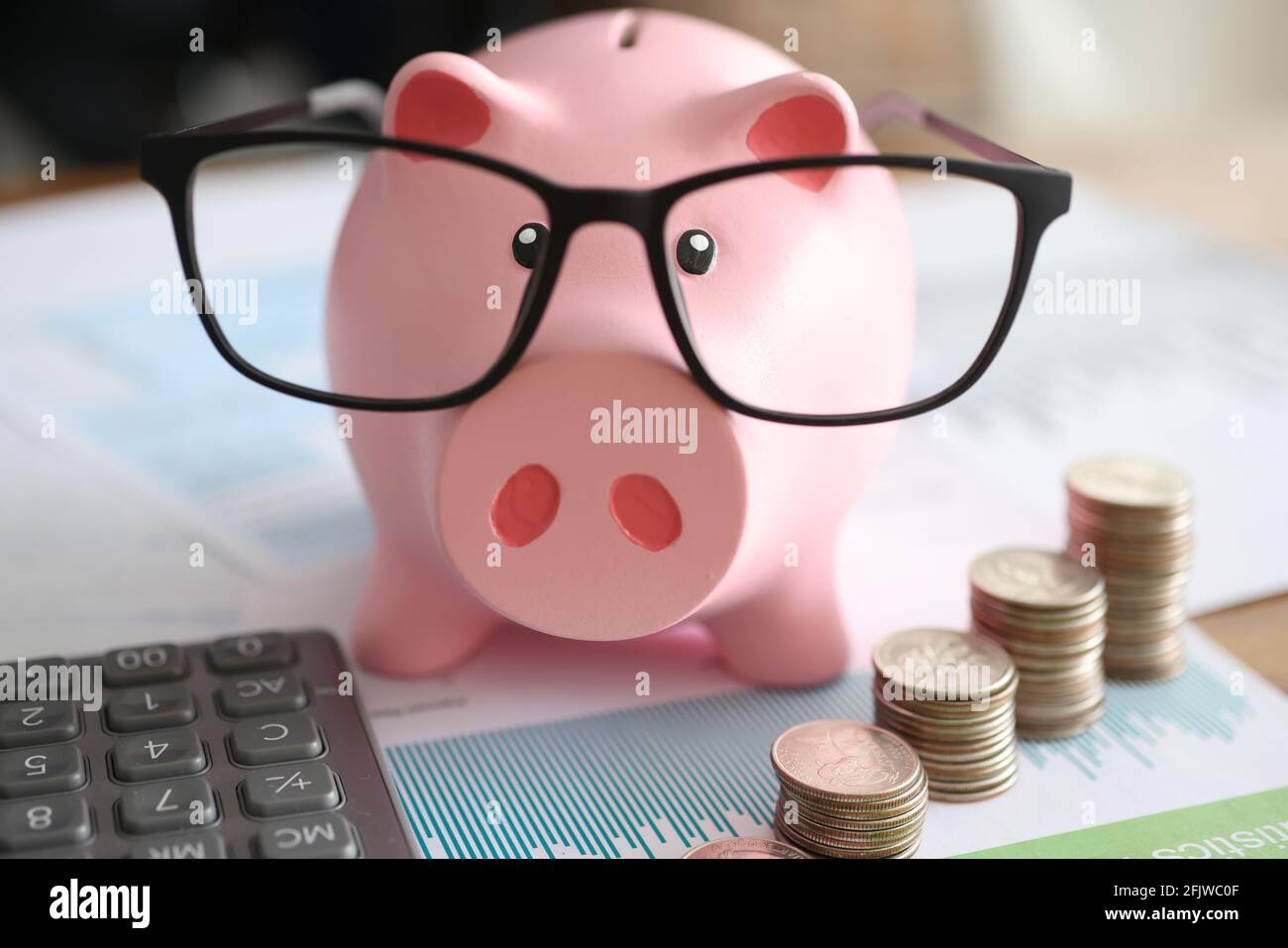 Porcellino rosa banca in occhiali vicino a business grafici e. monete Foto Stock