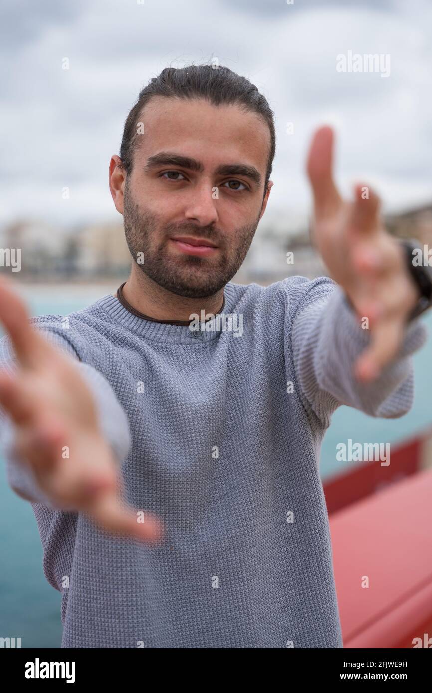 Uomo con le braccia allungate che raggiungono per qualcosa. Indossa un orologio da polso, un maglione grigio e una collana. Sta guardando avanti mentre prova Foto Stock