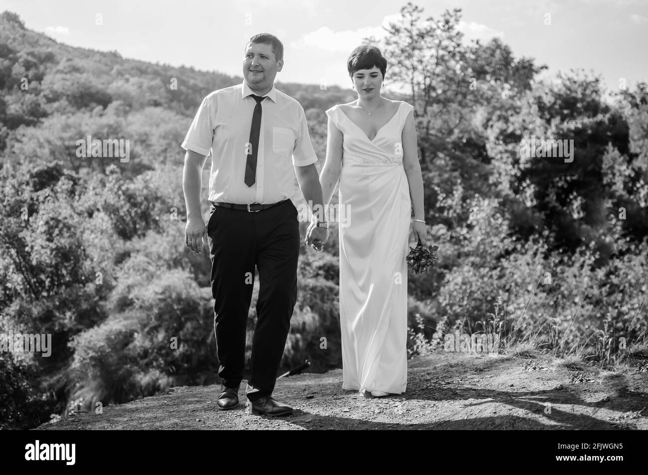 Gli sposi novelli tengono le mani sullo sfondo della foresta. Un uomo che tiene la mano di una donna Foto Stock