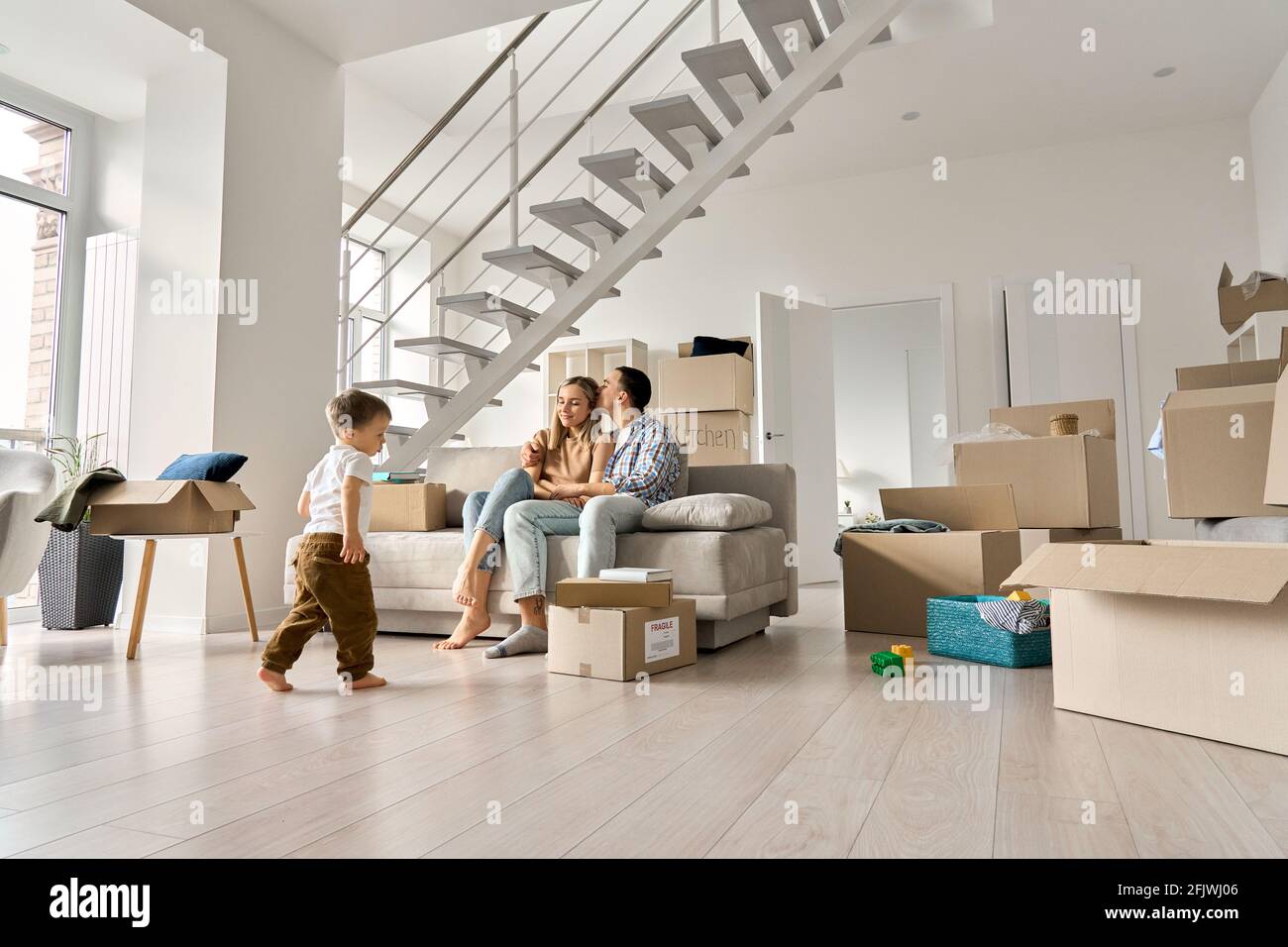 Famiglia felice rilassarsi sul divano in movimento giorno con bambino figlio giocare in nuova casa . Foto Stock