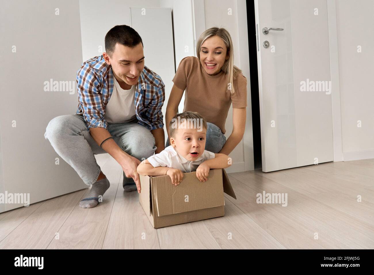 Divertente figlio eccitato cavalcare in scatola il giorno in movimento con i genitori in nuova casa. Foto Stock