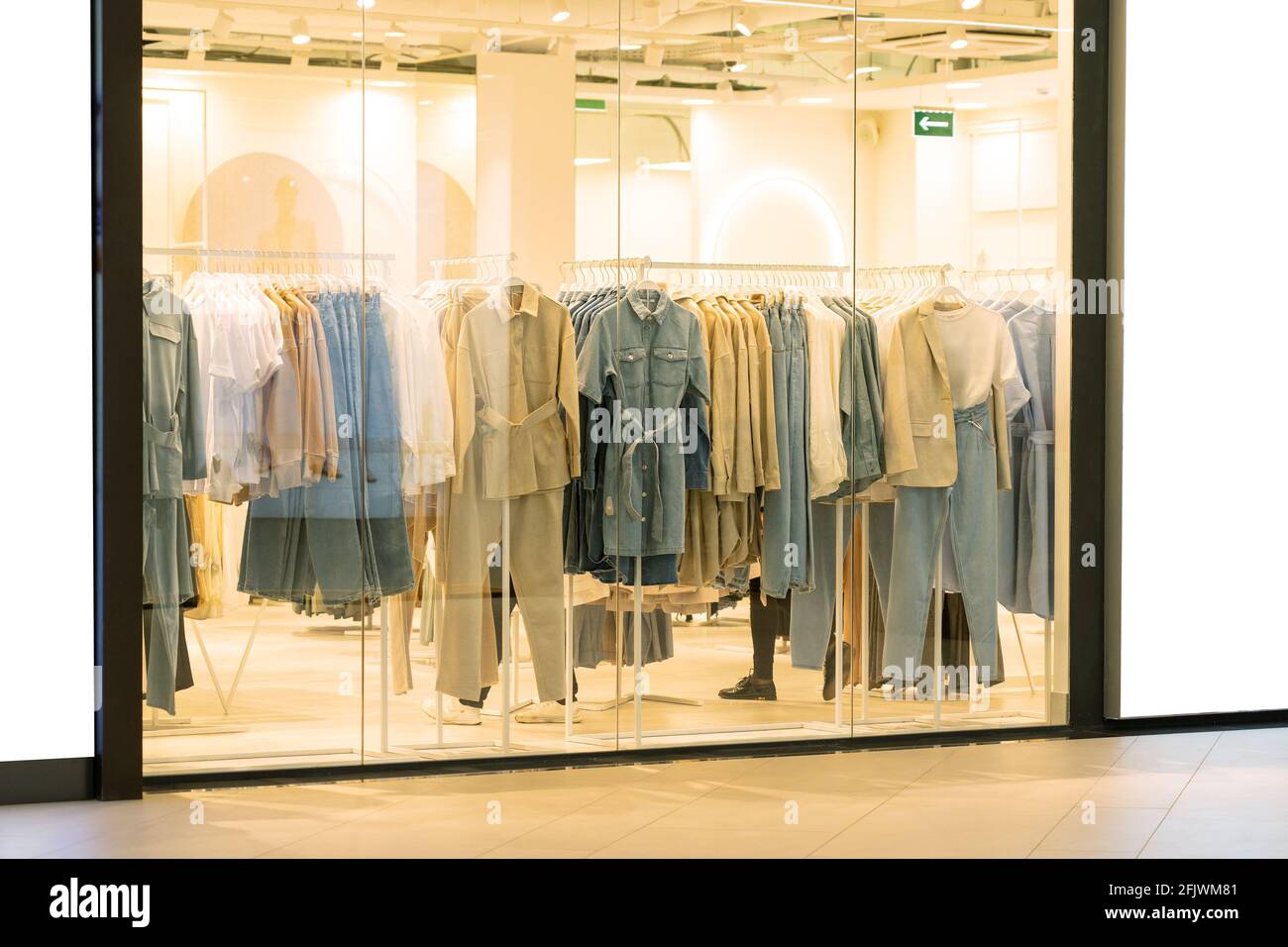 Vetrina con abbigliamento femminile in negozio di abbigliamento, nessuno. Cappotti, giacche e scarpe in boutique di moda Foto Stock