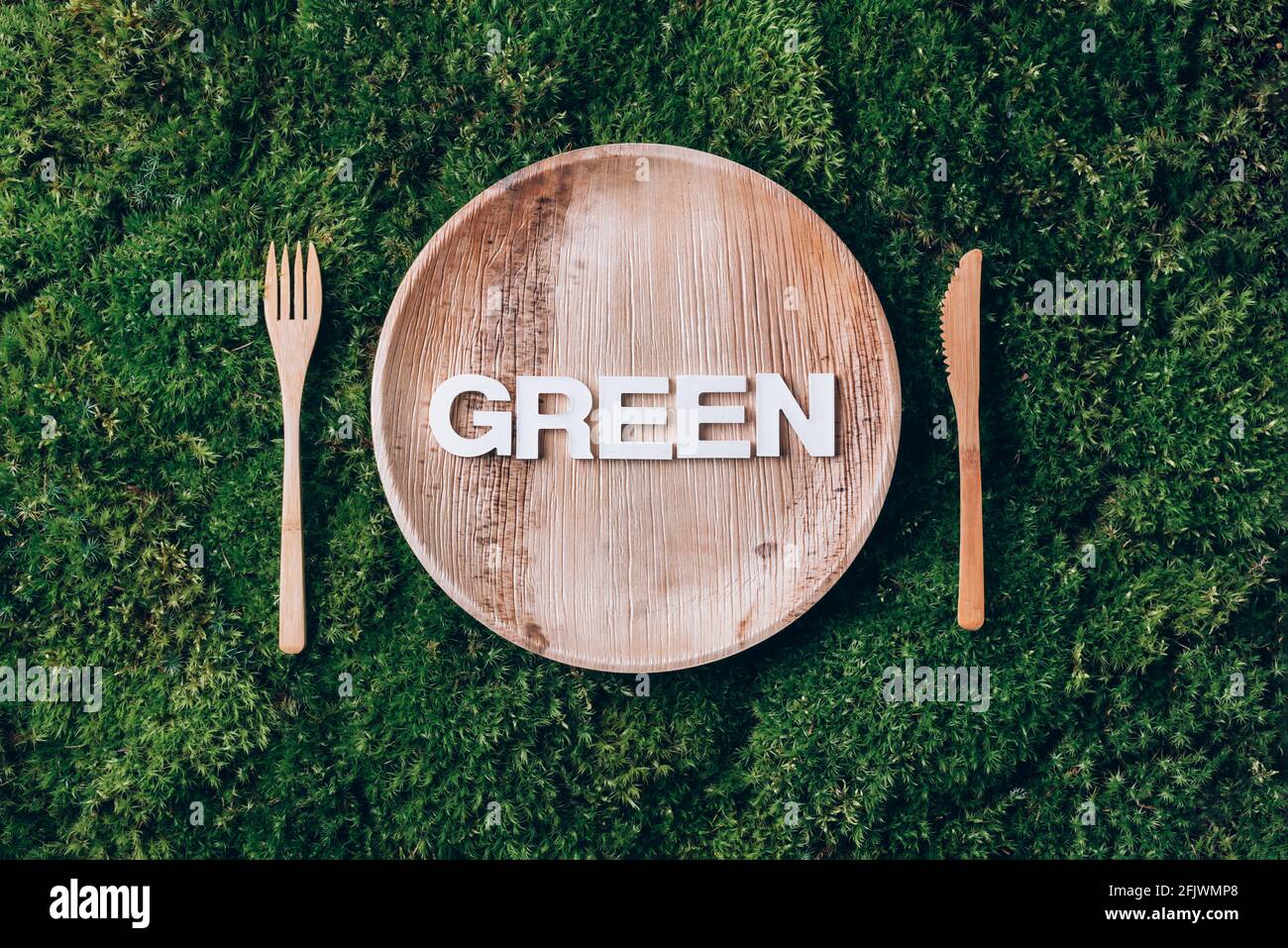 Stoviglie monouso in legno di materiali naturali con parola VERDE, cucchiaio di legno, forchetta su fondo di muschio verde. Stile di vita sostenibile ed ecologico Foto Stock