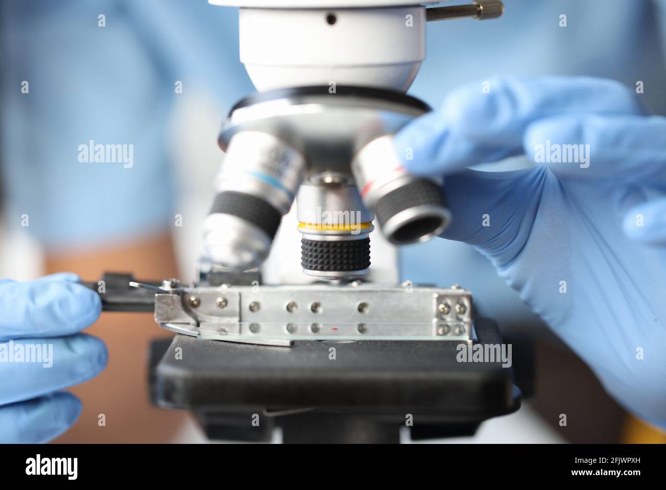 Mani di un ricercatore che conduce analisi del sangue al microscopio. Foto Stock