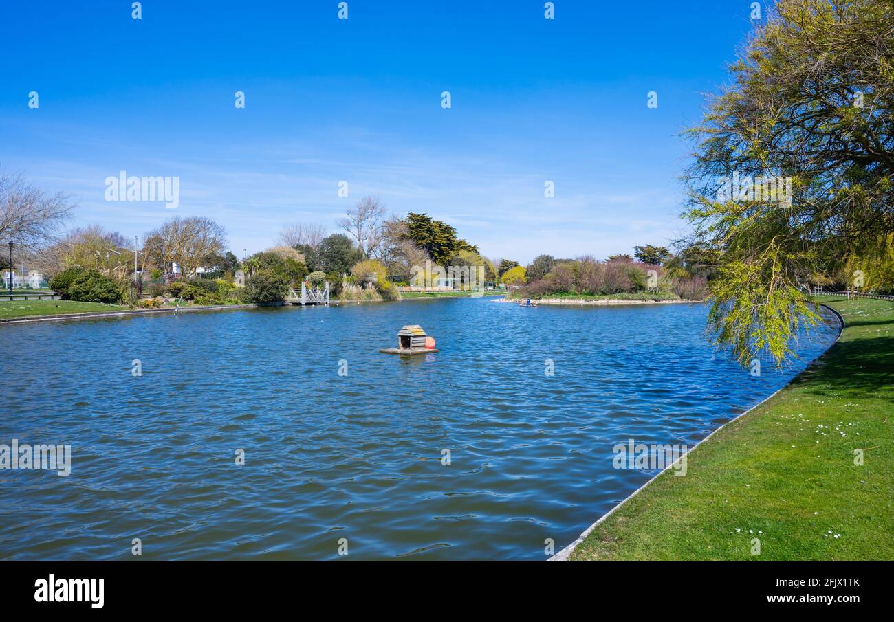 Vista del piccolo lago per la nautica con acque ancora blu in primavera a Mewsbrook Park, Littlehampton, West Sussex, Inghilterra, Regno Unito. Foto Stock