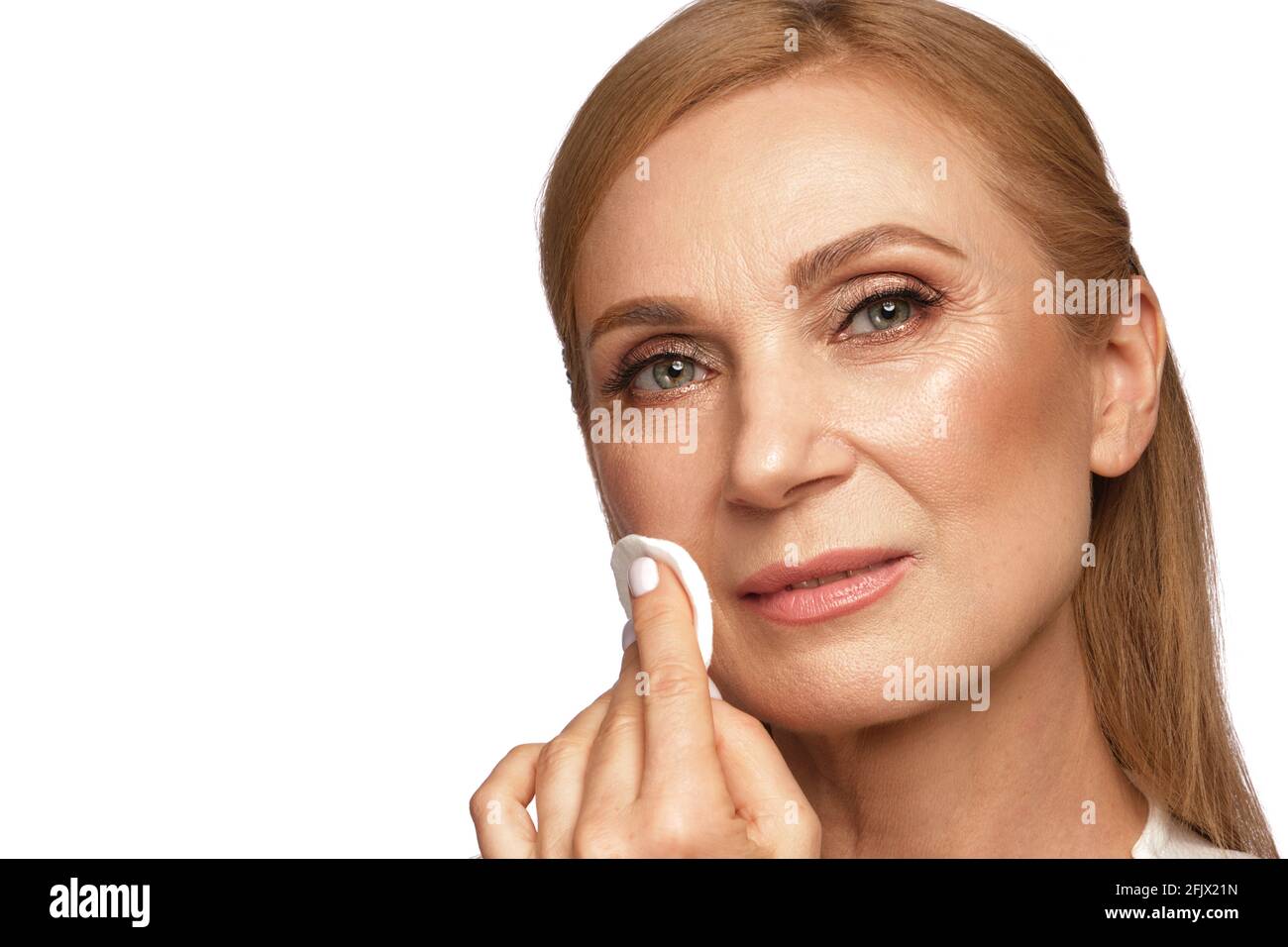 Ritratto di una bella donna anziana in una camicia bianca che rimuove il trucco con un detergente e un tampone di cotone. Foto Stock