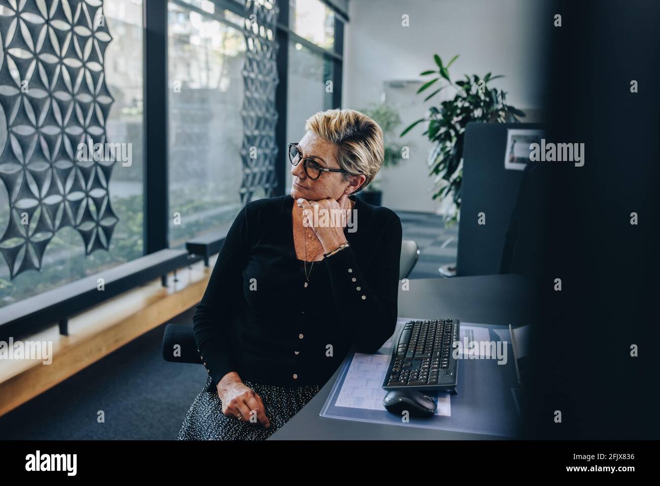 Professionista aziendale seduto alla sua scrivania guardando via con la mano sul mento. Donna d'affari stressata che si rilassa alla sua scrivania. Foto Stock