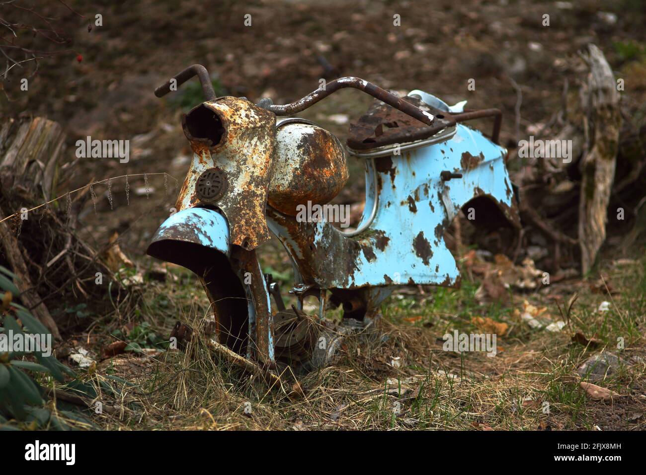 Abbandonato arrugginito vintage vecchia spazzatura ciclomotore cornice. Colore blu usurato e sbiadito con sfondo marrone sfocato. Foto Stock