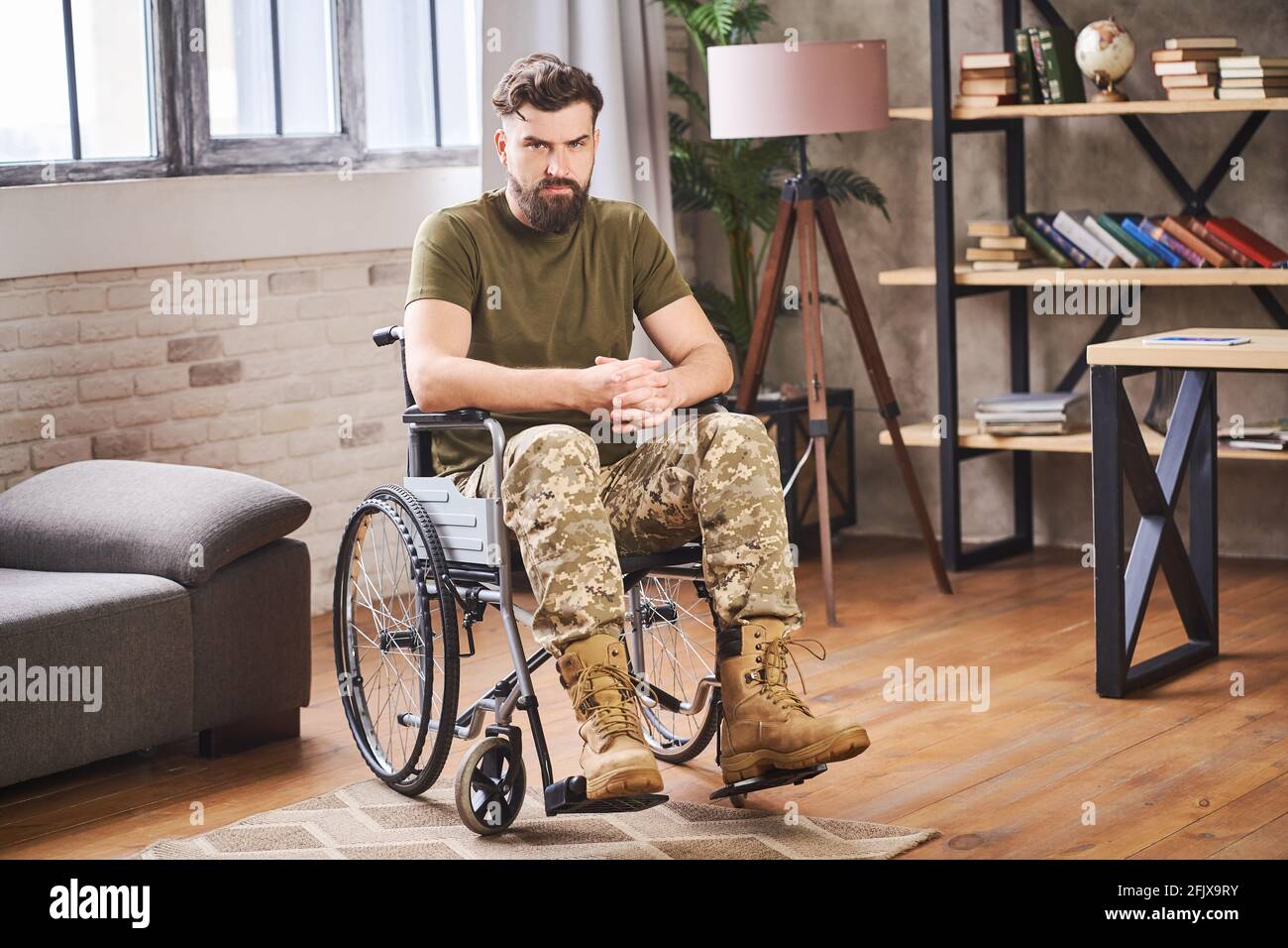 Giovane veterano con portatori di handicap seduto su una sedia a rotelle e guardando alla fotocamera Foto Stock