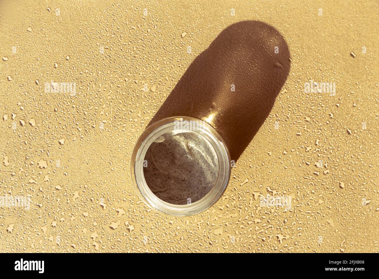 Maschera di scrub cosmetica per viso e corpo in vaso di vetro su tavolo beige bagnato con forti ombre. Medicina alternativa, prodotto di cura della pelle di bellezza. Vista dall'alto Foto Stock