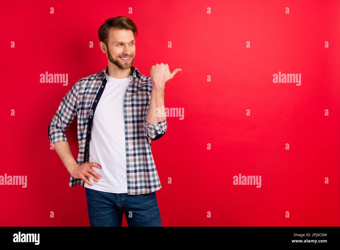 Foto di giovane uomo felice sorriso positivo sguardo pollice punto spazio vuoto consiglia consigli ad isolato su sfondo rosso Foto Stock