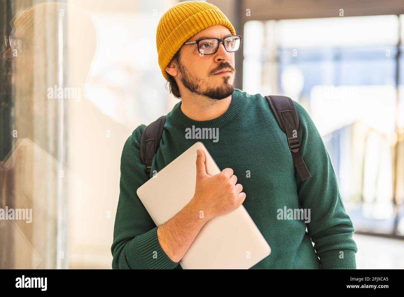 Uomo spagnolo moderno con occhiali e computer portatile in posa per lo shopping centro commerciale Foto Stock