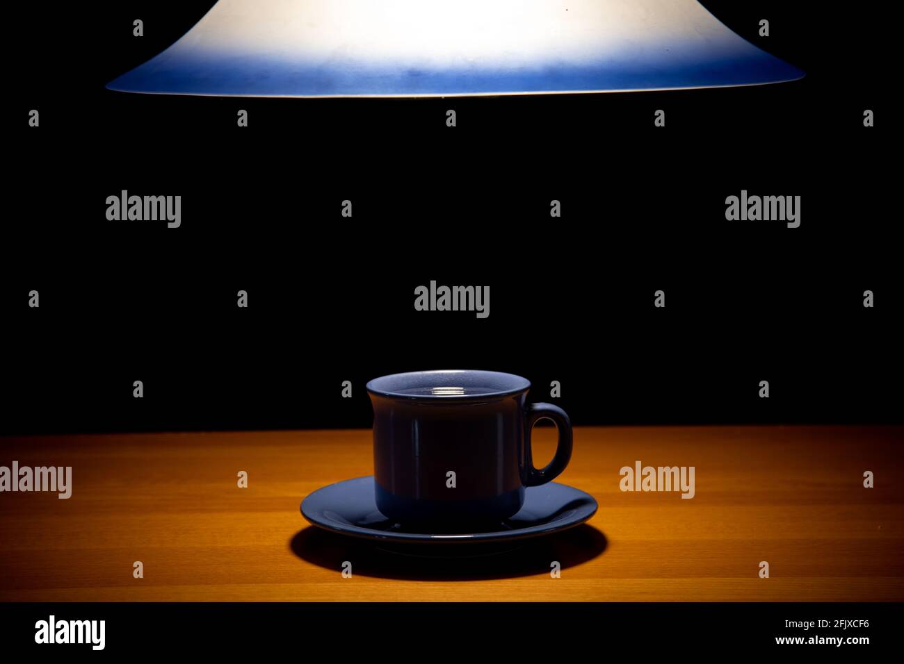 Un teacup sul tavolo sotto un lampadario di luce, su uno sfondo nero Foto Stock