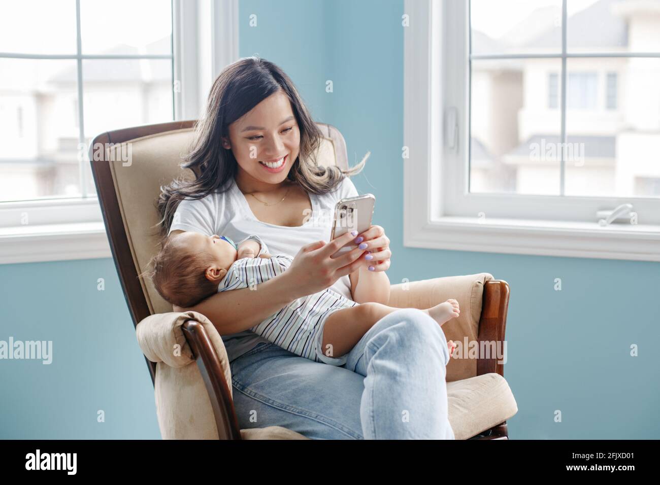 Madre asiatica che tiene il bambino neonato figlio e chiacchiera sopra smartphone Foto Stock