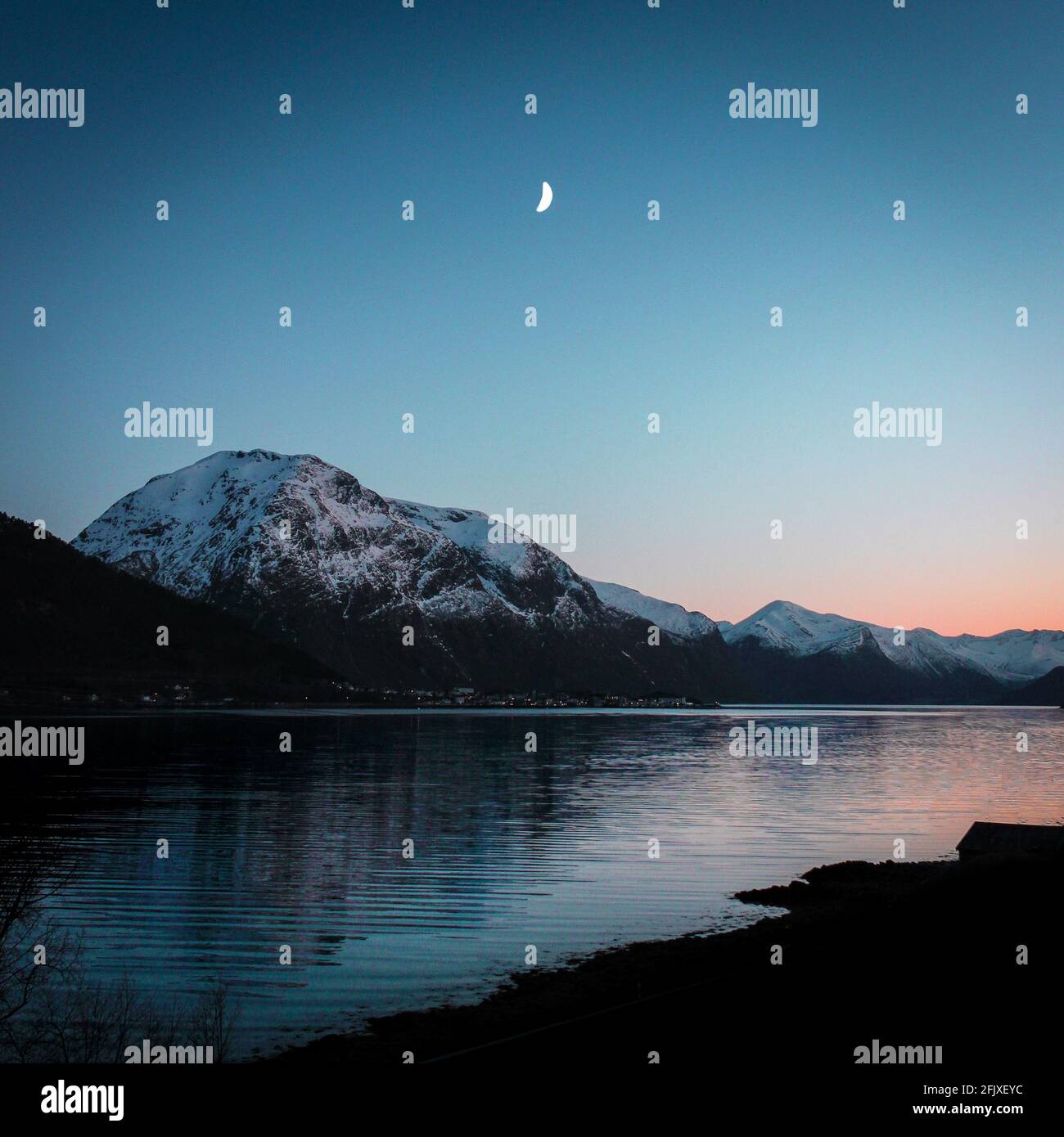 Tramonto in un fiordo norvegese con luna e montagne innevate Foto Stock