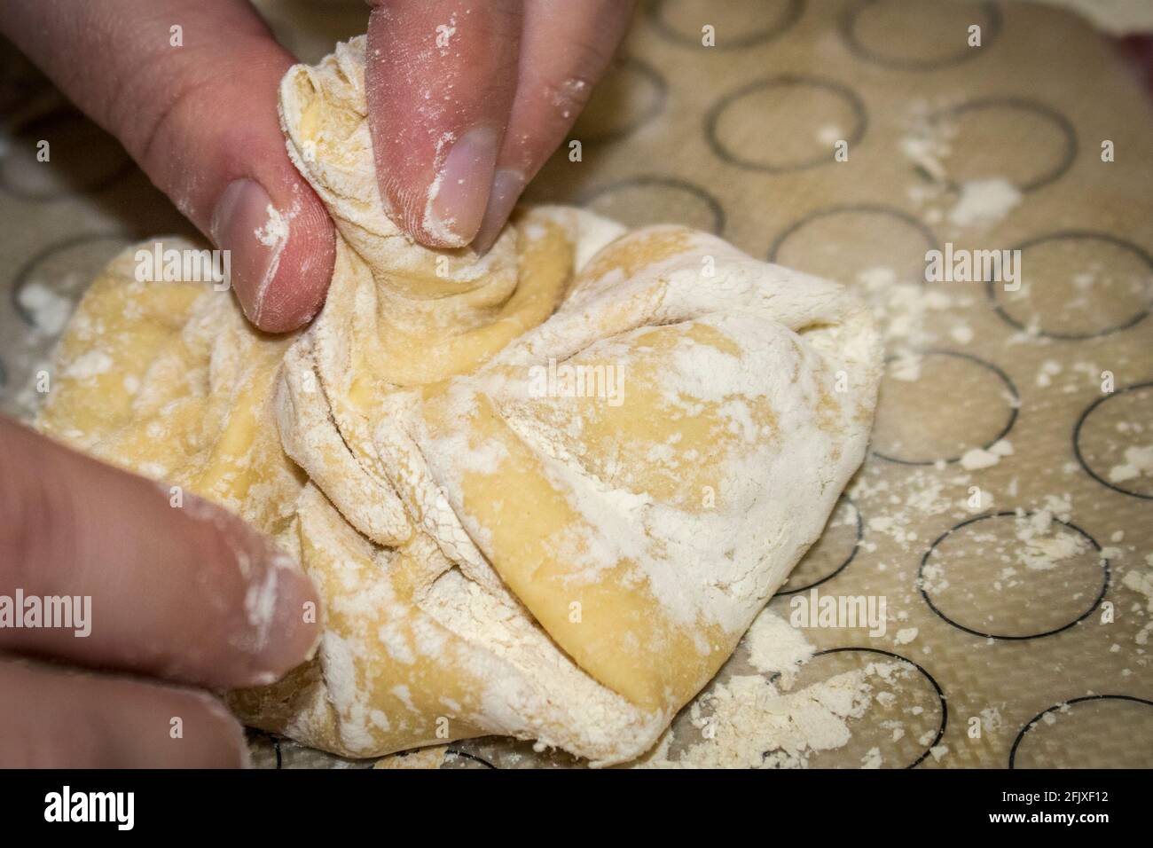 Mani che ruotano la manopola dell'impasto su un gnocco Khinkali ricoperta di farina su un tappetino di silicone - fuoco selettivo Foto Stock