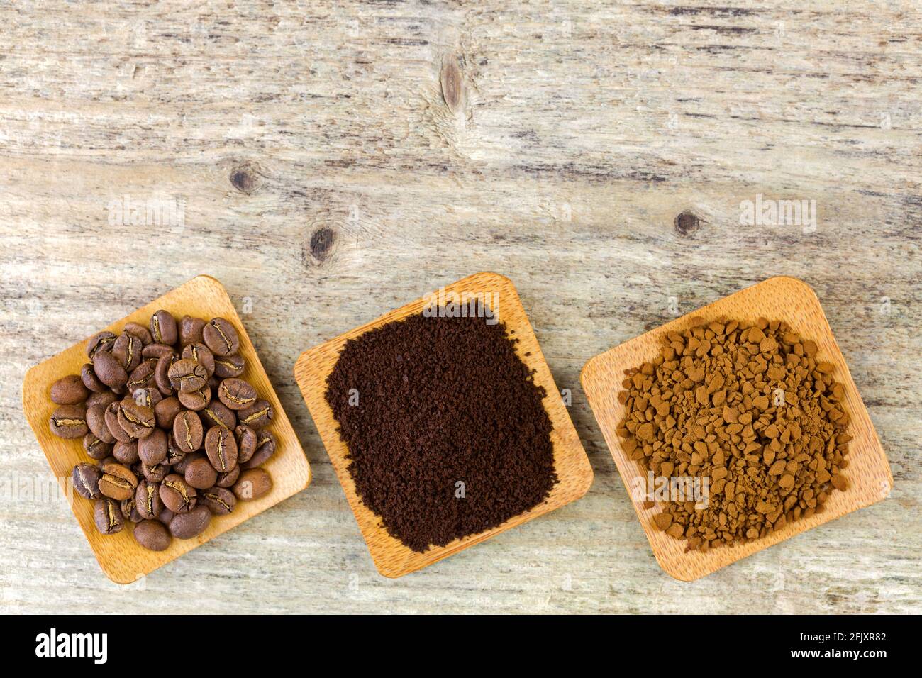 Chicchi di caffè arrosto, caffè macinato, caffè istantaneo granulare in ciotola, su sfondo di legno, vista dall'alto Foto Stock