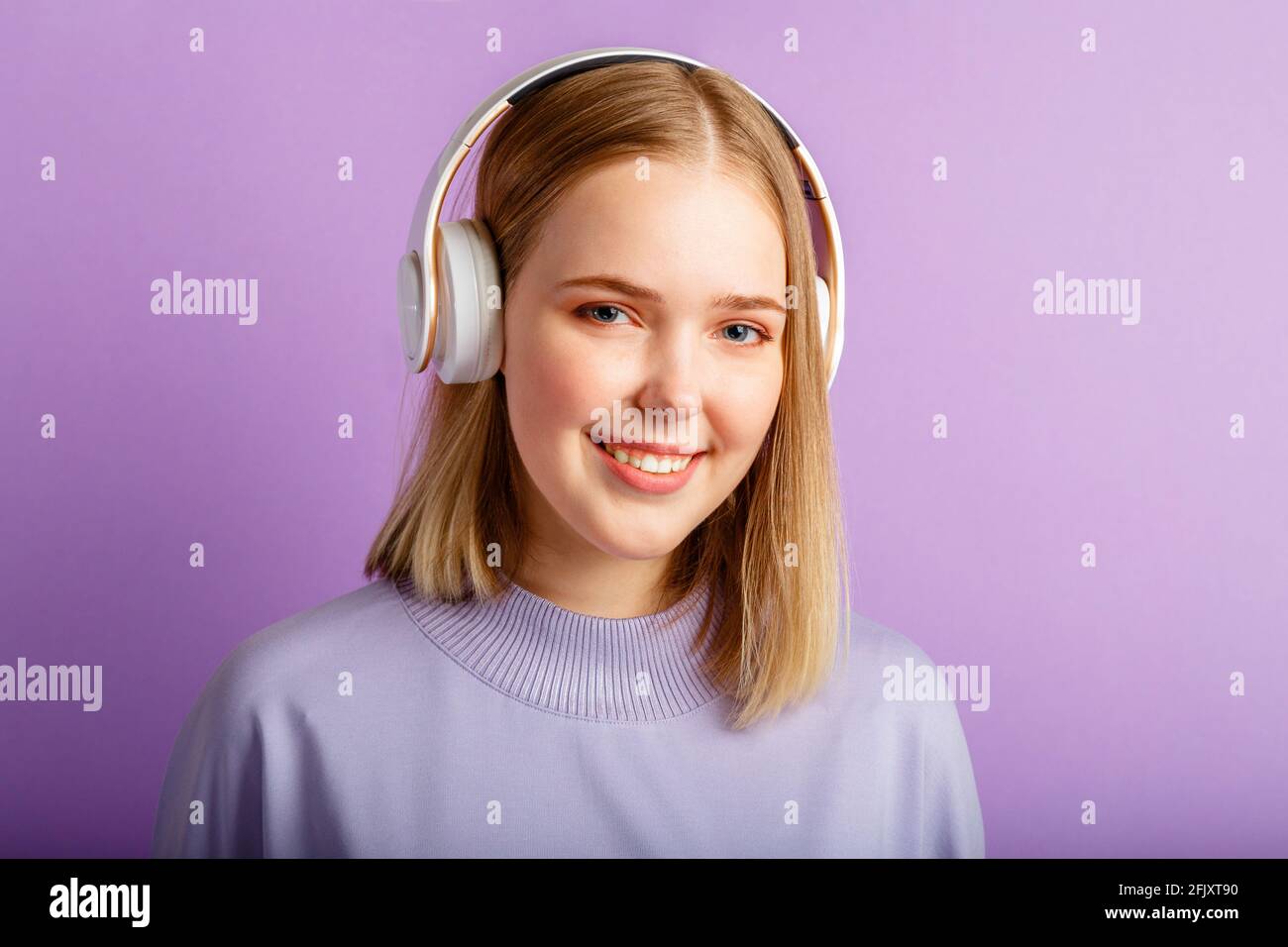 Felice giovane donna in cuffia ritratto. Bella donna sorridente con acconciatura bionda Ascolta musica song in cuffia isolata su viola Foto Stock