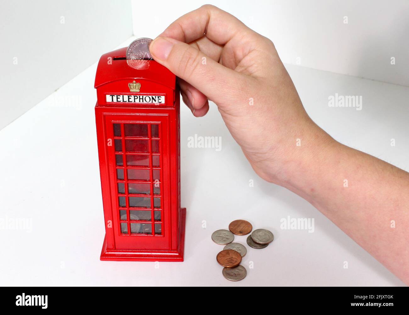 La mano della donna deposita monete in una London Phone Booth Coin Bank. Cabina telefonica britannica rossa. Banco di piggy. Foto Stock
