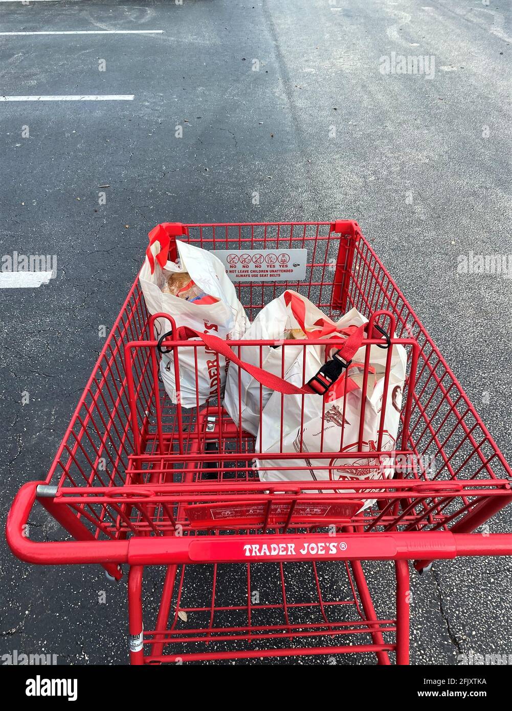 Carrello acquisti rosso con generi alimentari all'esterno di un negozio Trader Joe's nel parcheggio. Foto Stock