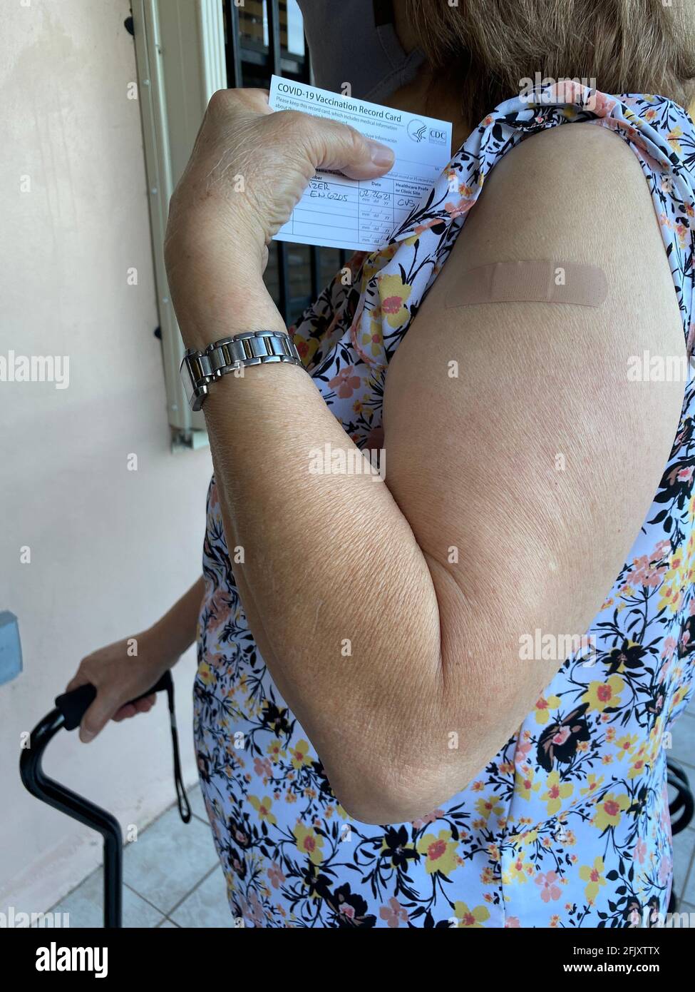 Felice donna anziana mascherata dopo aver ricevuto il vaccino Covid-19 presso la sua farmacia locale mostrando in mano la scheda di vaccinazione COVID-19 da parte del CDC. Foto Stock