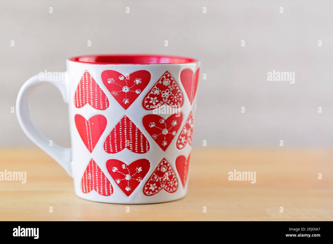 Tazza bianca su sfondo di legno. Tazza con motivi a forma di cuore su sfondo sfocato Foto Stock