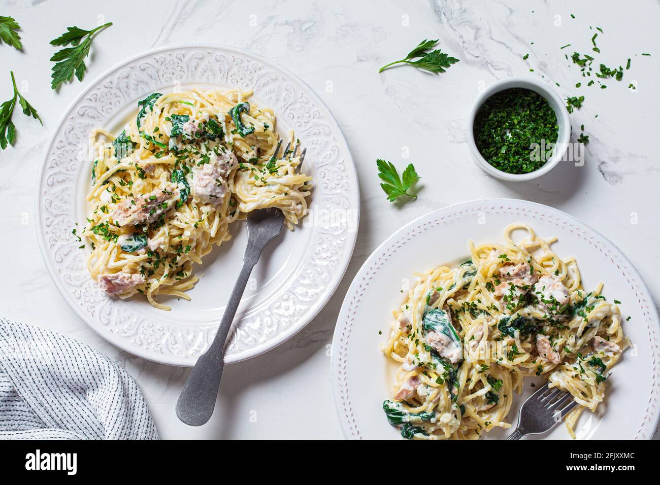 Spaghetti al tonno, spinaci e salsa cremosa su un piatto bianco con erbe, fondo in marmo bianco. Foto Stock