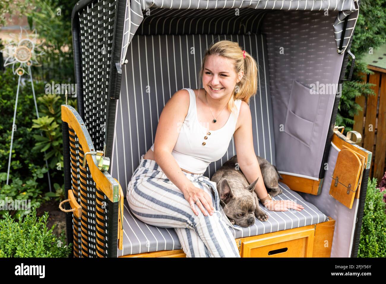 Giovane bionda seduta con il suo cane in proprio sedia da spiaggia in giardino Foto Stock