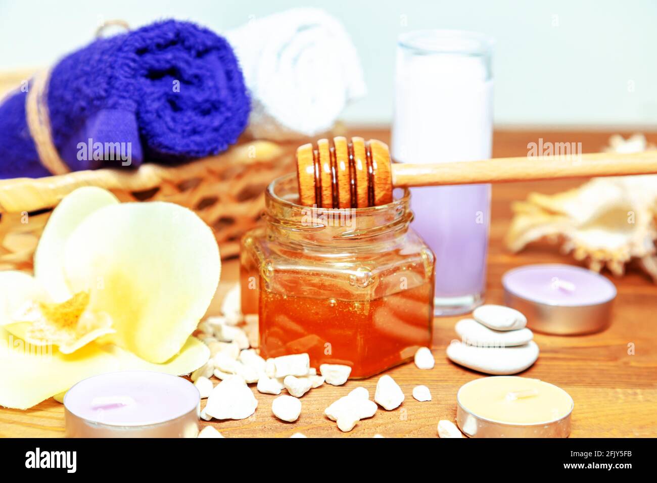Trattamento benessere al miele. Vaso miele dorato, fiori di orchidee, asciugamani e candele aromatiche. Cura naturale della pelle domestica. Foto Stock