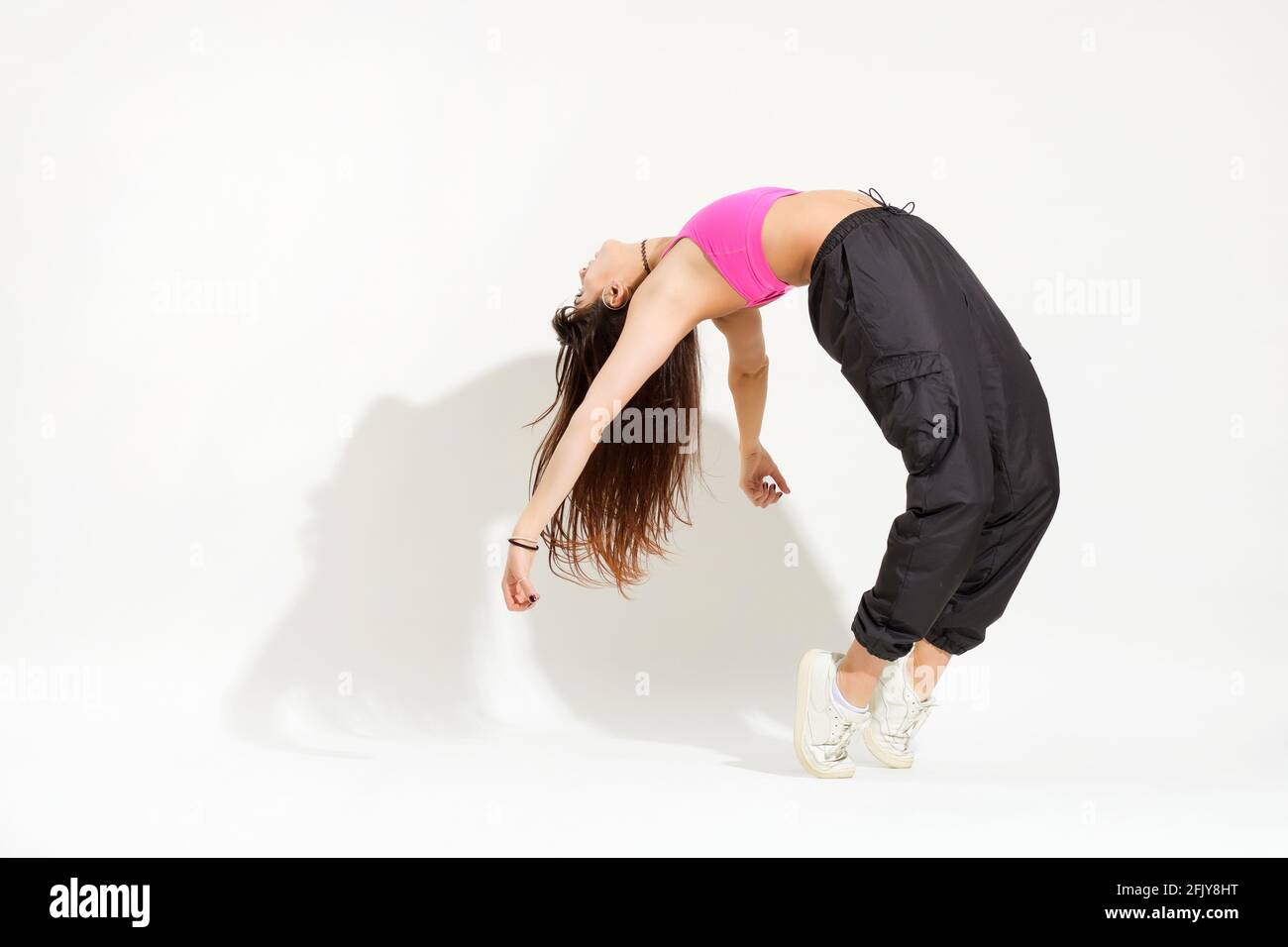 Donna flessibile hip hop ballerina isolato su bianco con ombra e copyspace come esegue una curva posteriore mentre si bilancia sulle sue dita Foto Stock