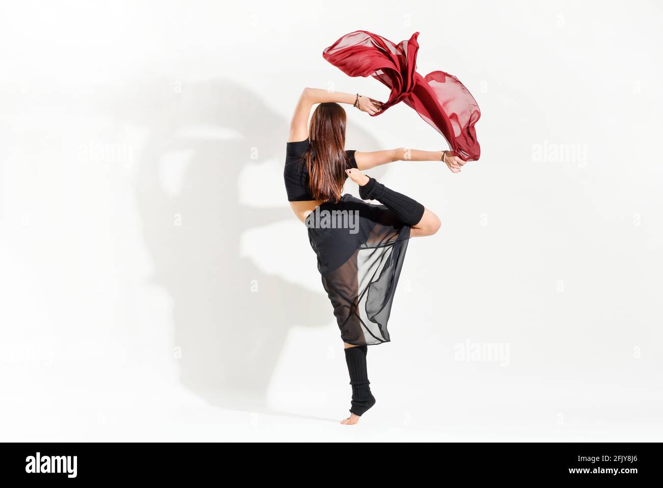 Ballerina donna che esegue una danza arabesca alternativa posa agitarsi con grazia tessuto rosso sopra la testa in una vista posteriore sopra bianco con ombra e co Foto Stock