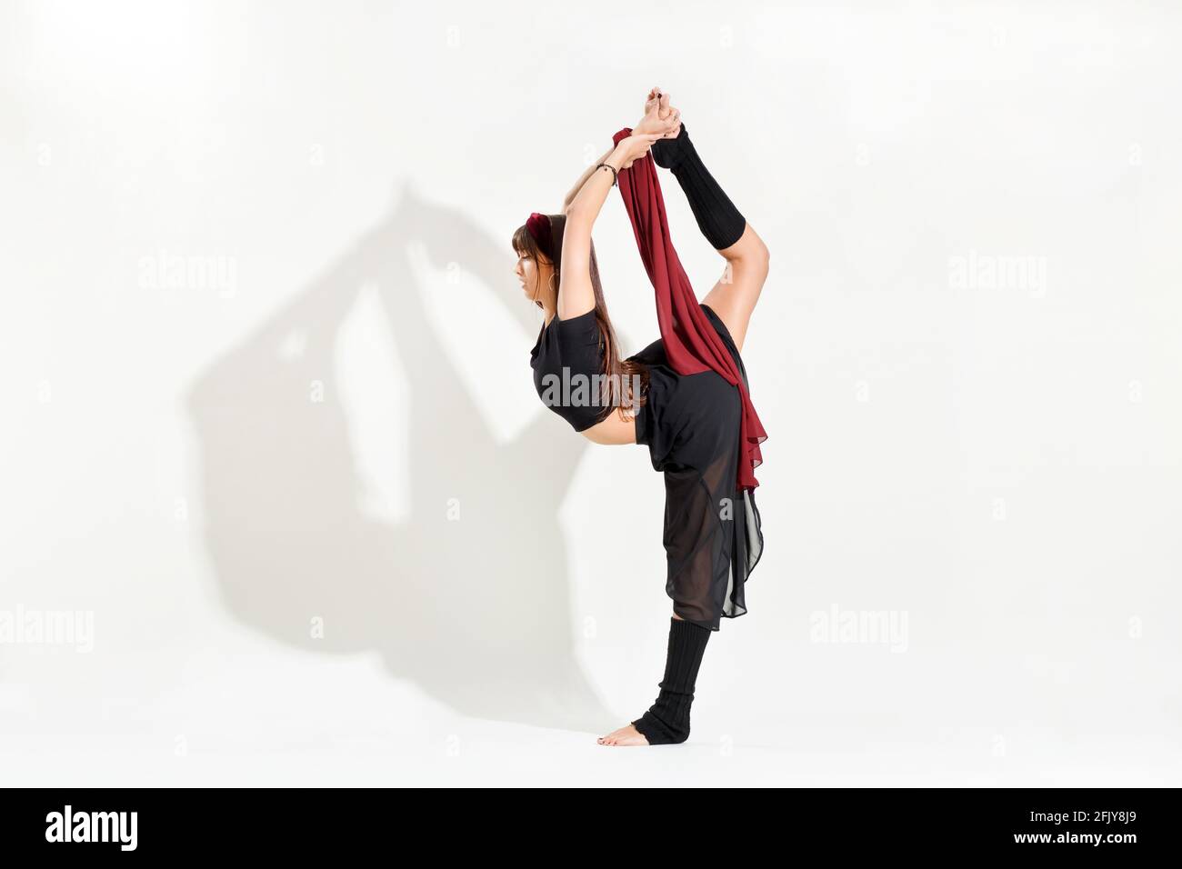 Giovane ballerina che esegue un pattinaggio su ghiaccio Biellman posa allungarsi afferrare il piede mentre si equilibrano su una gamba dentro una vista laterale isolata su bianco con Foto Stock