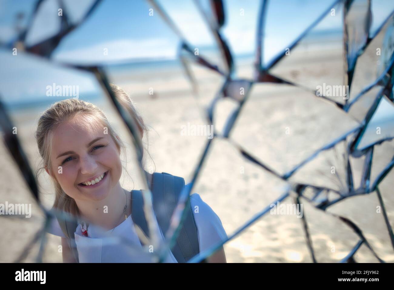 Riflesso di una ragazza bionda sorridente in uno specchio rotto - Foto Stock