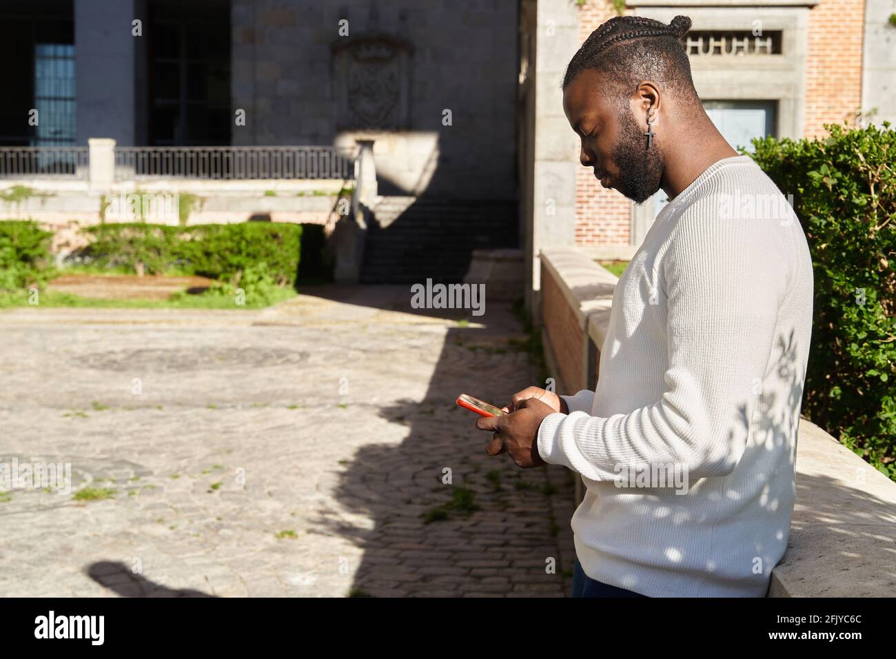 Bell'uomo afro-americano che chiacchiera tramite smartphone in piedi, allegro uomo dalla pelle scura godendo di tempo libero blogging in reti tramite smartphone. Foto di alta qualità Foto Stock